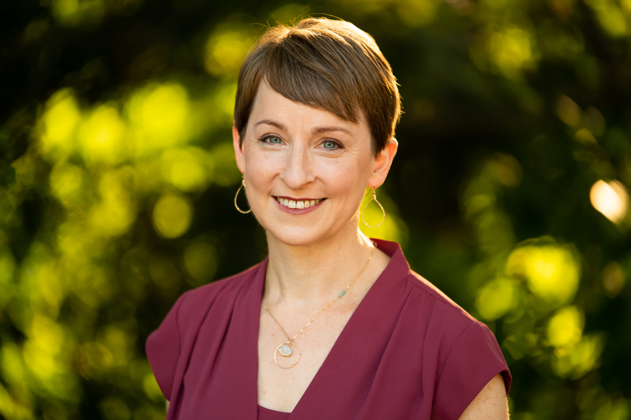 Photograph of white woman smiling against background of trees